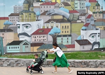 A woman pushes a stroller with her son in front of a mural in Kyiv.