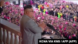 Стоп кадър от държавната телевизия на Северна Корея. Видеото е излъчено на 10 октомври 2020 г. То показва реч на лидера Ким Чен Ун преди началото на военен парад. Хиляди граждани и военни дефилират без предпазни маски.