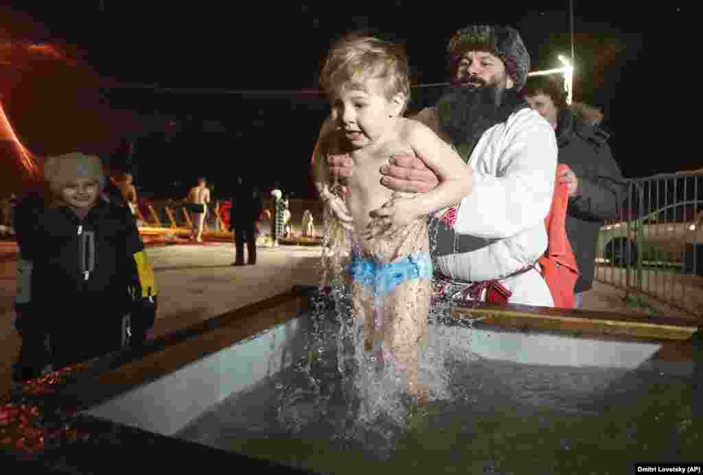 A man plunges a boy into frigid water in St. Petersburg, Russia.