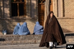 Afghan burqa-clad women sit along a pavement in the Gazargah area of Herat on January 7.