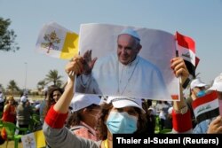 Një grua mban një fotografi të Papa Françeskut, në afërsi të Aeroportit të Bagdadit, ndërsa pret që ai të arrijë.