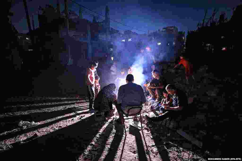 Palestinians sit around a fire between their families destroyed houses in Beit Hanun town northern Gaza Strip on May 26, 2021.&nbsp;