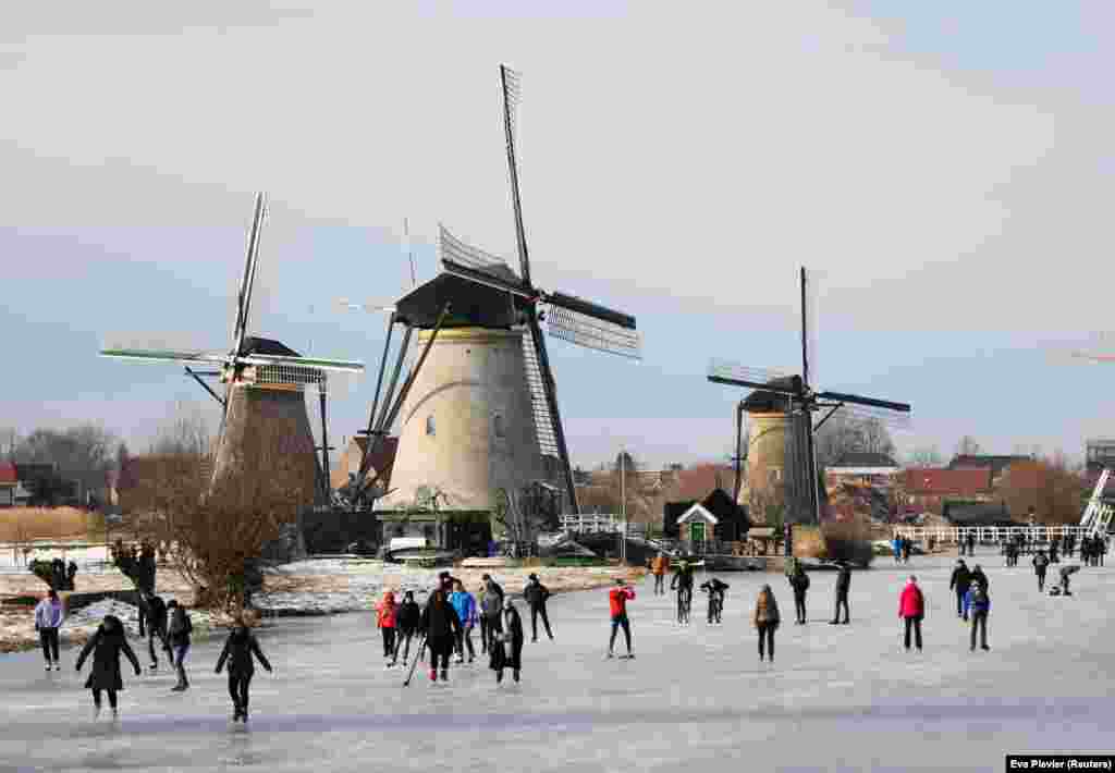 Korcsolyázó emberek a holland Kinderdijk szélmalmok környékén.