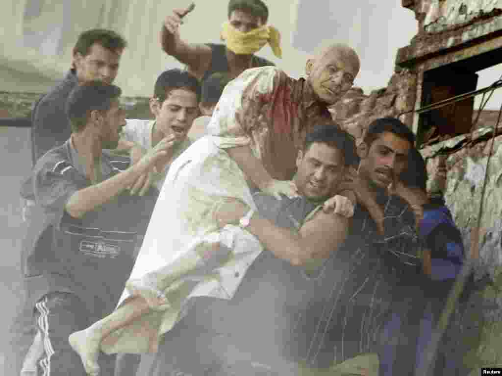 I - Rescuers carry a wounded man from the rubble of a building demolished by a bomb in the centre of the Iraqi capital of Baghdad June 14, 2004. A suicide car bomber blew himself up on a busy Baghdad street on Monday as a convoy of foreigners in civilian cars drove past, partly demolishing a nearby building, police at the scene said. REUTERS/Faleh Kheiber 