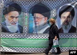 A woman in Tehran walks past a banner bearing the images of former Iranian supreme leaders Ayatollah Ruhollah Khomeini (left), Ayatollah Ali Khamenei (center), and his son, the current supreme leader, Mojtaba Khamenei.