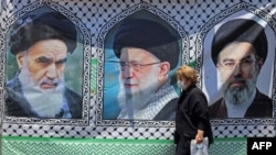 A woman in Tehran walks past a banner bearing the images of former Iranian supreme leaders Ayatollah Ruhollah Khomeini (left), Ayatollah Ali Khamenei (center), and his son, the current supreme leader, Mojtaba Khamenei. 