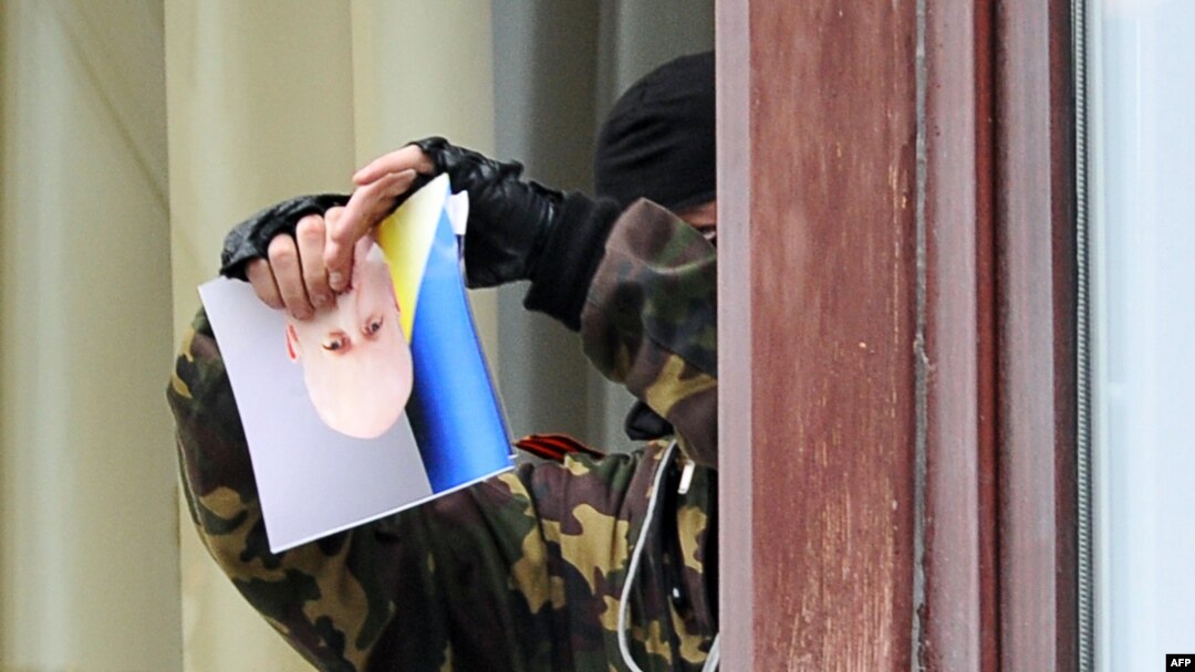 A pro-Russian activist rips a photo of interim President Oleksandr Turchynov as he stands at a window of the regional administration building in Luhansk.