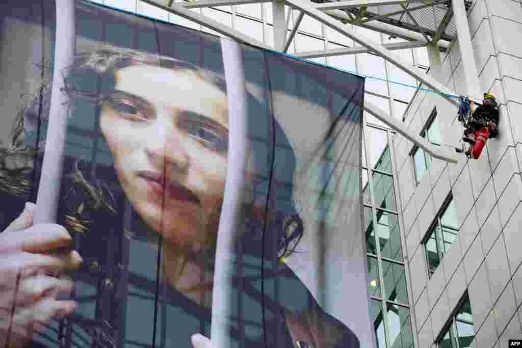 Members of Greenpeace hang a large poster of Dutch activist Faiza Oulahsen on the office building of Shell during a protest calling for the release of the &quot;Arctic 30&quot; in Rotterdam on November 21. Oulahsen was one of&nbsp;30 people from 18 countries who were arrested after a protest in September at a Gazprom oil rig in the Arctic. (AFP/Martijn Beekham)