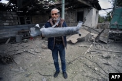 A man displays a shell fragment in the yard of his brother's house,, which was damaged by shelling during fighting between Armenia and Azerbaijan over the breakaway Nagorno-Karabakh region, in the region's city of Martuni on October 1.