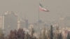 The Iranian flag flutters over the capital blanketed in winter's heavy smog pollution, in Tehran on November 25 2025. (Photo by ATTA KENARE / AFP)