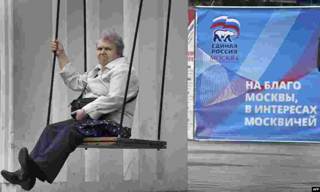 A woman rides on a swing next to an election poster for the United Russia party in central Moscow ahead of the country&#39;s parliamentary elections, which are scheduled for September 18. (AFP/Alexander Nemenov)