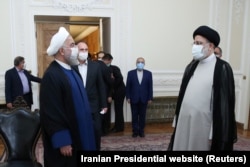 Former Iranian President Hassan Rohani (left) stands as he hands over the powers of his office to ultraconservative Ebrahim Raisi (right) in Tehran in August 2021.