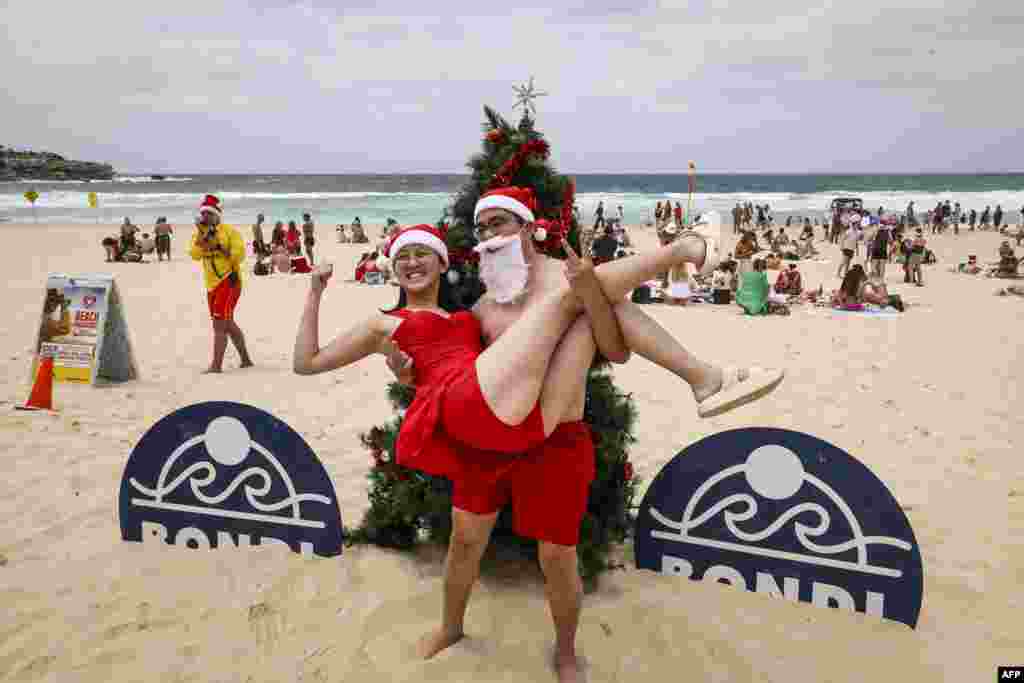 Turistë me kostume krishtlindjesh fotografohen para pemës së Krishtlindjes në plazhin Bondi në Sidnej.