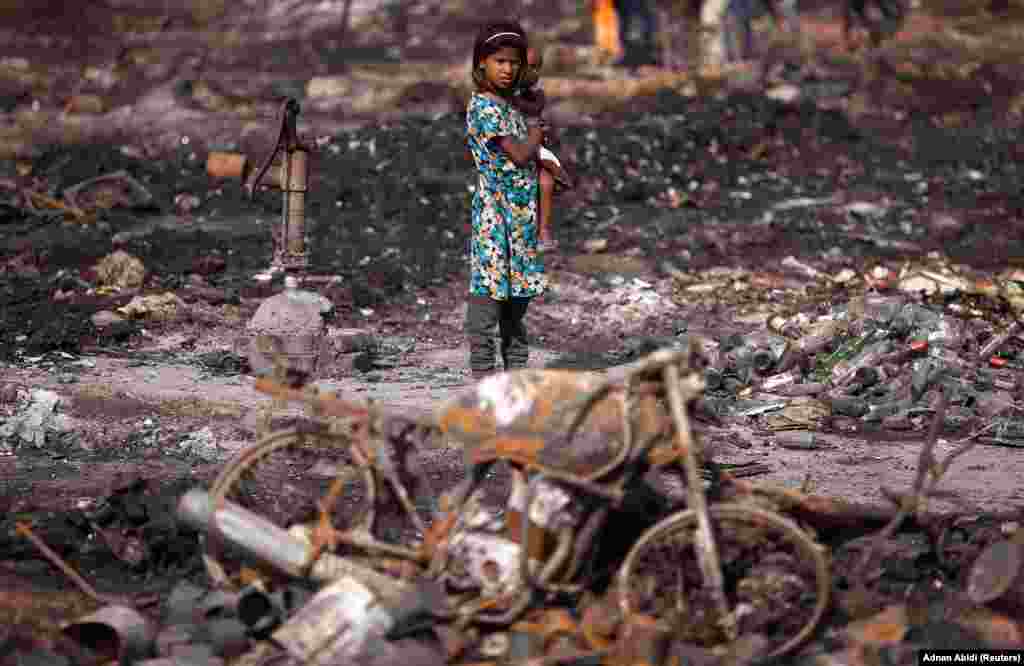 A girl carries her brother as she stands near her burnt home after a fire broke out in a slum area in New Delhi on April . (Reuters/Adnan Abidi)&nbsp;