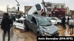 People stand near a pile of damaged cars after a flood hit the city of Shiraz on March 25.