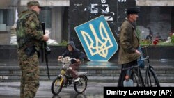 Egy fiú biciklizik az orosz szeparatistáktól visszafoglalt Szlovjanszkban. Az épület előtt az ukrán címerrel.