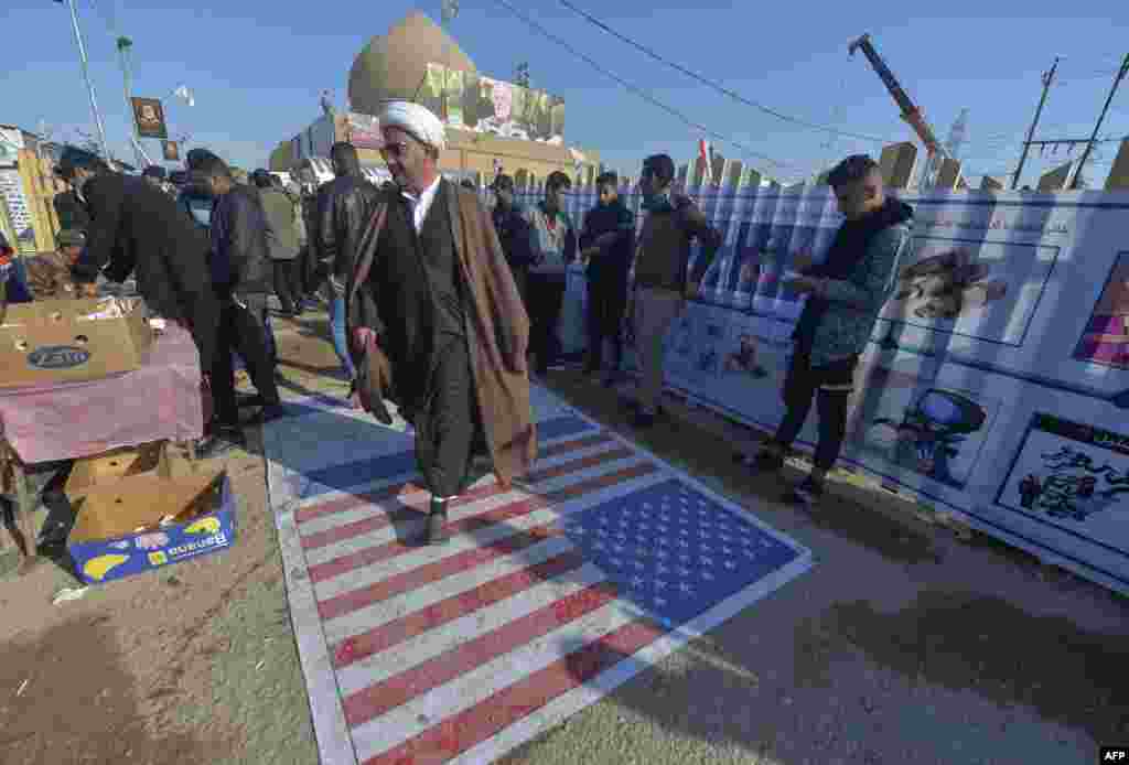 An Iraqi cleric walks on a U.S. flag painted on the ground as people gather to pay respects by the grave of slain commander Abu Mahdi al-Muhandis at the Wadi al-Salam cemetery in the holy city of Najaf on January 4, marking the first anniversary of his killing alongside Islamic Revolutionary Guards Corps commander Qasem Soleimani in a U.S. drone strike. (AFP/Ali Najafi)