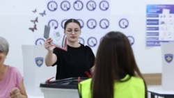 Një zyrtare e Komisionit Qendror të Zgjedhjeve vëzhgon teksa një qytetare e hedh votën e saj në kutinë e votimit në zgjedhjet e parakohshme parlamentare të 7 qershorit, në një qendër votimi në Prishtinë, 7 qershor 2026.