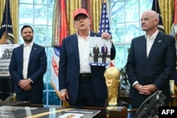 Donald Trump, flancat de vicepreședintele american JD Vance (stânga) și președintele FIFA, Gianni Infantino, ține în mână o fotografie cu el și președintele rus Vladimir Putin în Alaska, în timp ce vorbește în Biroul Oval al Casei Albe, la Washington, DC, pe 22 august 2025.