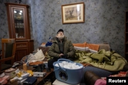 Сяргей Пржыстоўскі сядзіць у сваім пакоі зь вядром сьнегу, які зьбіраецца растапіць за ноч. Ягоная кватэра засталася бяз вады пасьля таго, як мінулай ноччу расейскі дрон ударыў па будынку падчас атакі на Кіеў, 10 студзеня 2026 году