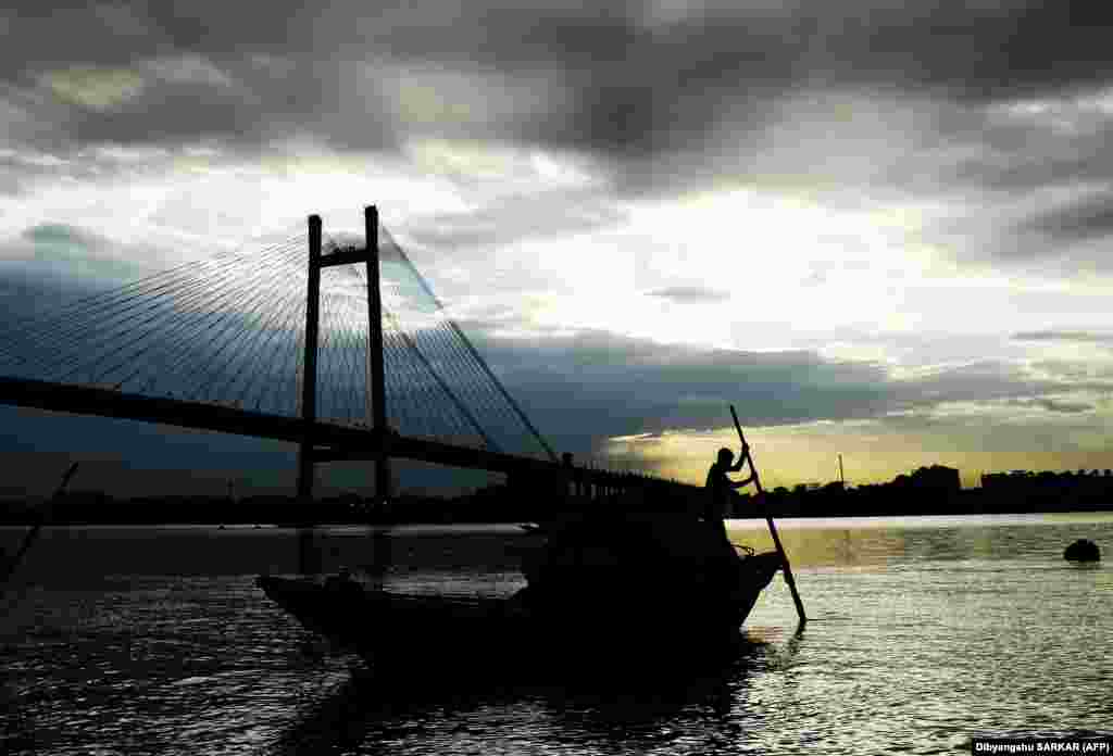 An Indian boatman transports tourists on the Ganges River as rain clouds loom, in Kolkata. (AFP/Dibyangshu Sarkar)