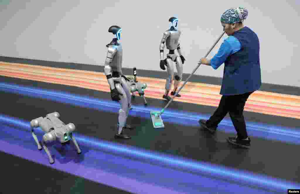 A woman cleans the floor next to robots during the Digital Almaty 2025 forum in Kazakhstan.