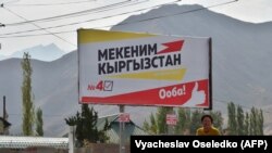 A woman walks in front of a campaign billboard for Mekenim Kyrgyzstan in the village of Koi-Tash, outside Bishkek.