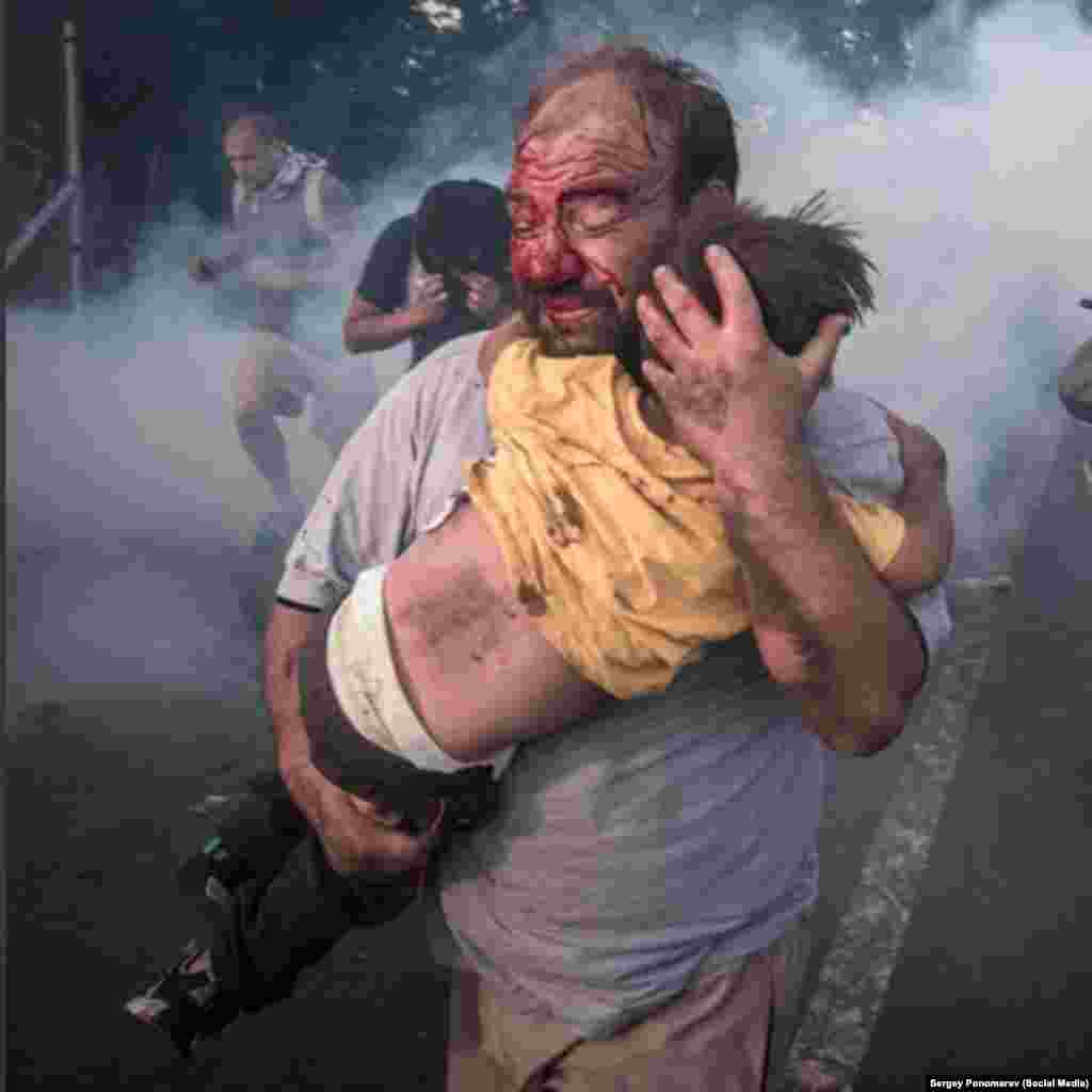 Мужчина несёт своего ребенка после того, как полиция применила слезоточивый газ и водомёты в ответ на попытку мигрантов пересечь границу с Венгрией