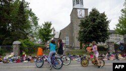Жители селения Канауаке в провинции Квебек останавливаются в молчании перед выставленной у стен церкви обувью – в память о 215 детях, чьи останки были найдены 30 мая 2021 года в Британской Колумбии на месте одного из интернатов