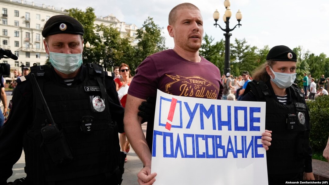 Russian police detain an opposition activist who is holding a poster reading "Smart Voting" in Moscow on August 14.
