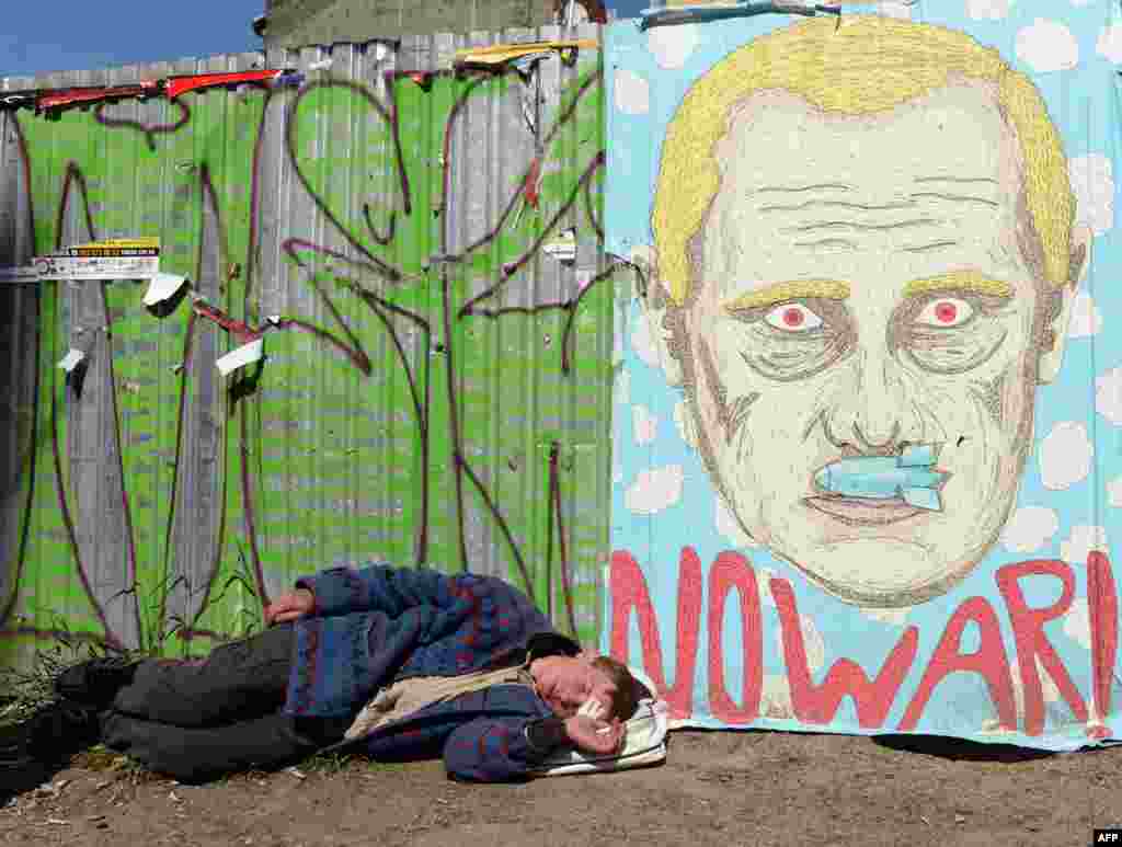 A man sleeps under an antiwar poster depicting Russian president Vladimir Putin with a bomb as a mustache in the center of the western Ukrainian city of Lviv. (AFP/Yuriy Dyachyshyn)