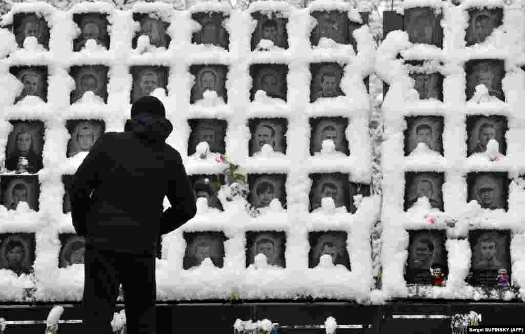 A man looks at images of the &quot;Heavenly Hundred&quot; Memorial commemorating people who died during Ukraine&#39;s Maidan protests of 2013-2014, after a heavy snowfall in Kyiv. (AFP/Sergei Supinsky)