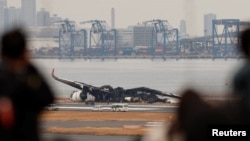 Oameni curioși contemplând la 3 ianuarie, o zi după accident, ce a mai rămas din avionul cuprins de flăcări pe aeroportul Haneda din Tokio (Foto: REUTERS/Issei Kato) 