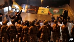 Supporters of the Iran-backed militant group hold the flags of Hezbollah and Amal Movement, as they stand in front of Lebanese army soldiers forming a barrier. November 25, 2019