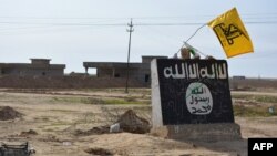 A flag of the Shi'ite Hizballah militant group flutters over a mural depicting the emblem of the Islamic State (IS) group in Al-Alam village, northeast of the Iraqi city of Tikrit, in early March.