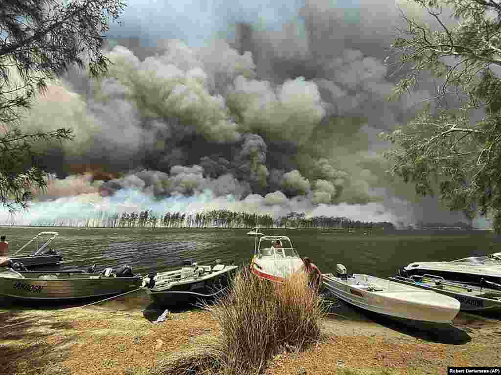 Boats are pulled ashore as smoke and wildfires rage behind Lake Conjola, Australia. Thousands of tourists fled Australia&#39;s wildfire-ravaged eastern coast ahead of worsening conditions as the military started to evacuate people trapped on the shore further south. The fires have killed at least 24 people and destroyed more than 1,200 homes. (AP/Robert Oerlemans)