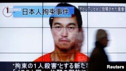 Жапон журналисі Кендзи Гото көрсетілген үлкен экранның қасынан өтіп жара жатқан адам. Токио, 25 қаңтар 2015 жыл.