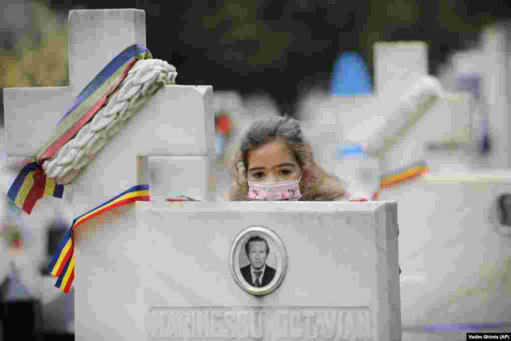 A Romanian child, wearing a mask for protection against the coronavirus, leans on the cross of a victim of the 1989 anti-communist revolution after a memorial religious service in Bucharest for those killed in the uprising. (AP/Vadim Ghirda)
