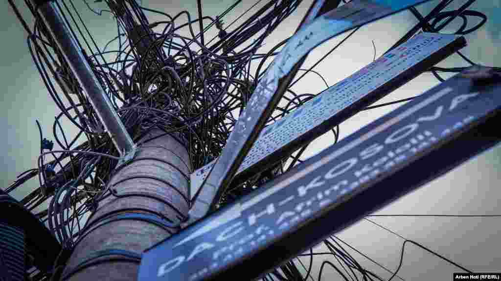 Kabllo të komunikimit dhe tela të rrymës të bëra lëmsh në një shtyllë betoni në një rrugë të kryeqytetit.