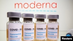 Vials with a sticker reading, "COVID-19 / Coronavirus vaccine / Injection only" and a medical syringe are seen in front of a displayed Moderna, October 31, 2020.