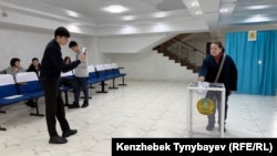 Өзінің дауыс берген сәтін смартфонына суретке түсіріп беруді өтінген әйелді фотоға түсіріп тұрған жігіт. Алматы, 15 наурыз, 2026 жыл.