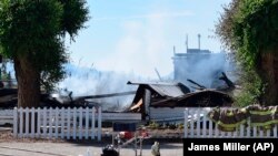 Jachetele pompierilor atârnă pe gardul rămășițelor arse ale Bisericii Sacred Heart de pe rezervația Penticton. Incendiile de luni, 21 iunie, au distrus două biserici.