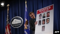 WASHINGTON, DC - MARCH 24: A Department of Justice employee put up a poster of the seven indicted hackers prior to a news conference for announcing a law enforcement action March 2