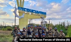 Бойцы теробороны Украины возле свежеперекрашенного (из цветов российского флага на украинский) въездного знака в освобожденном от российской армии поселке Шевченково Харьковской области. 10 сентября 2022 года