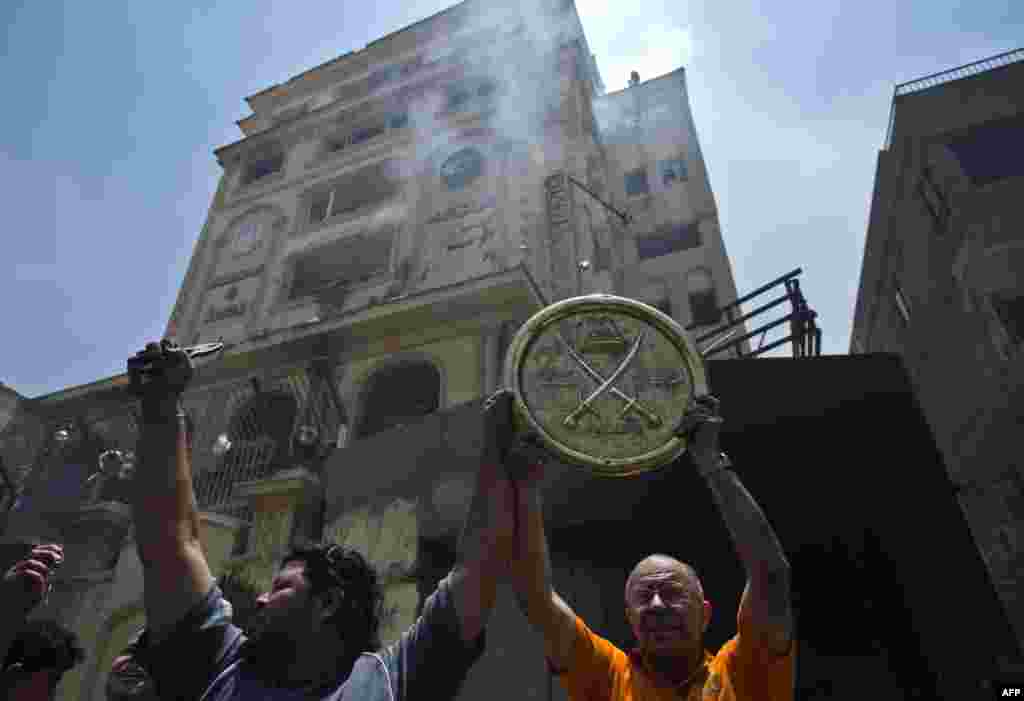 Protesters hold up an emblem of the Muslim Brotherhood removed from the party&#39;s headquarters, which was looted and set on fire by angry crowds.