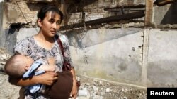 An ethnic Uzbek woman and her infant child pass a burned-out house after the fierce ethnic clashes on the outskirts of Osh, in southern Kyrgyzstan, in late June.