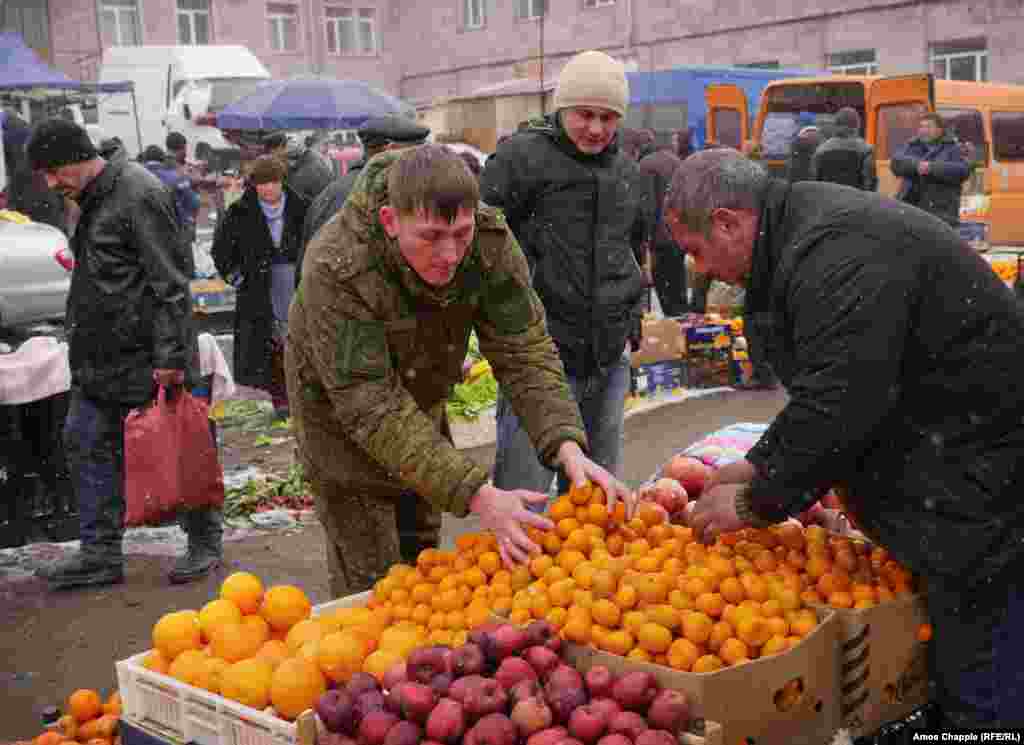 Российский военнослужащий покупает мандарины на центральном рынке Гюмри. Во время расследования убийства семьи Аветисян было выявлено масштабное хищение продуктов, предназначавшихся Минобороны России для питания своих военнослужащих в Армении. Все продукты были украдены и потом вновь перепроданы на местных рынках.