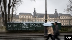 Pietoni trec pe lângă tarabele verzi închise ale unui "bouquiniste" parizian (librarii de cărți second-hand și anticariat) acoperite cu graffiti, pe malul stâng al Senei, în timp ce Louvre se vede în fundal, în Paris, la 7 februarie 2024.