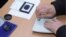 Armenia - An official at a polling station in Yerevan puts a special stamp on a voter's passport which is supposed to prevent multiple voting, 18Feb2013.