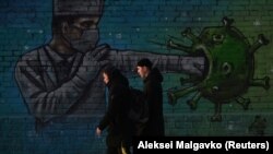 People in Omsk walk past graffiti depicting a health-care worker fighting the coronavirus as the pandemic sweeps through Russia. 